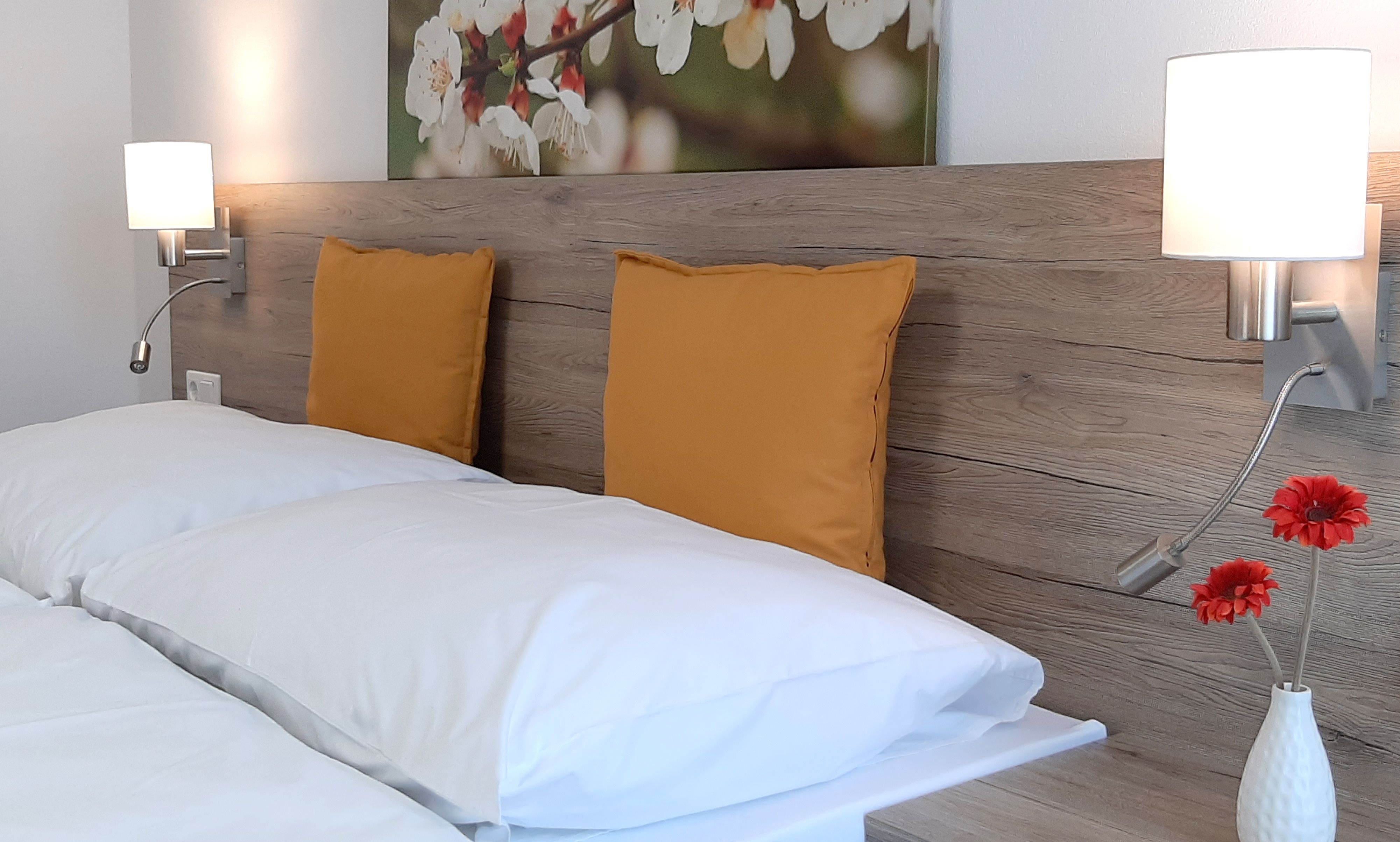 Double bed with wooden back panel, yellow cushions and wall lamps.