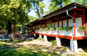 A red building with changing rooms and plants in front of it, surrounded by trees and people on benches.