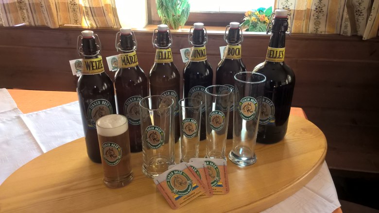 Various Fiaker Bräu beer bottles and glasses on a table.