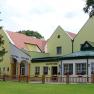 Yellow building with hotel and restaurant, surrounded by trees and lawn.