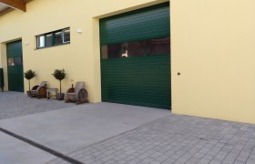 Yellow building with green gates and wooden furniture outside.