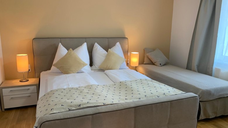 Comfortable bedroom with double bed and single bed, two bedside lamps and curtains.