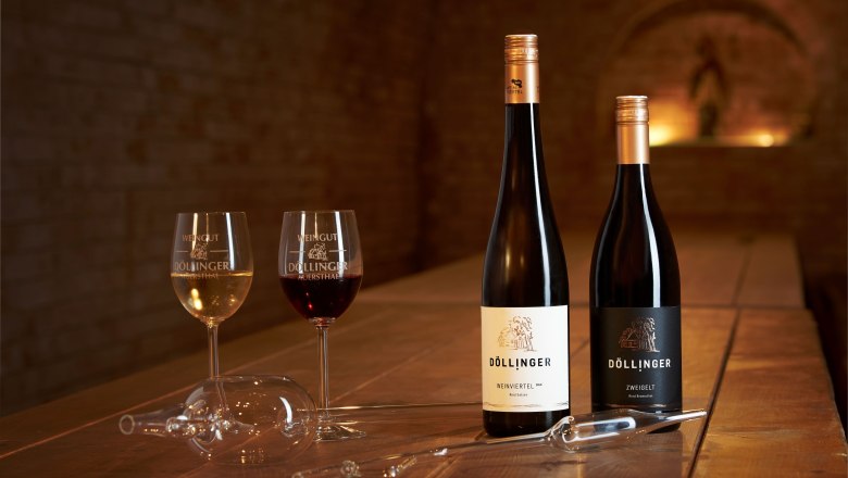 Two wine glasses and two bottles of wine on a wooden table in a wine cellar.