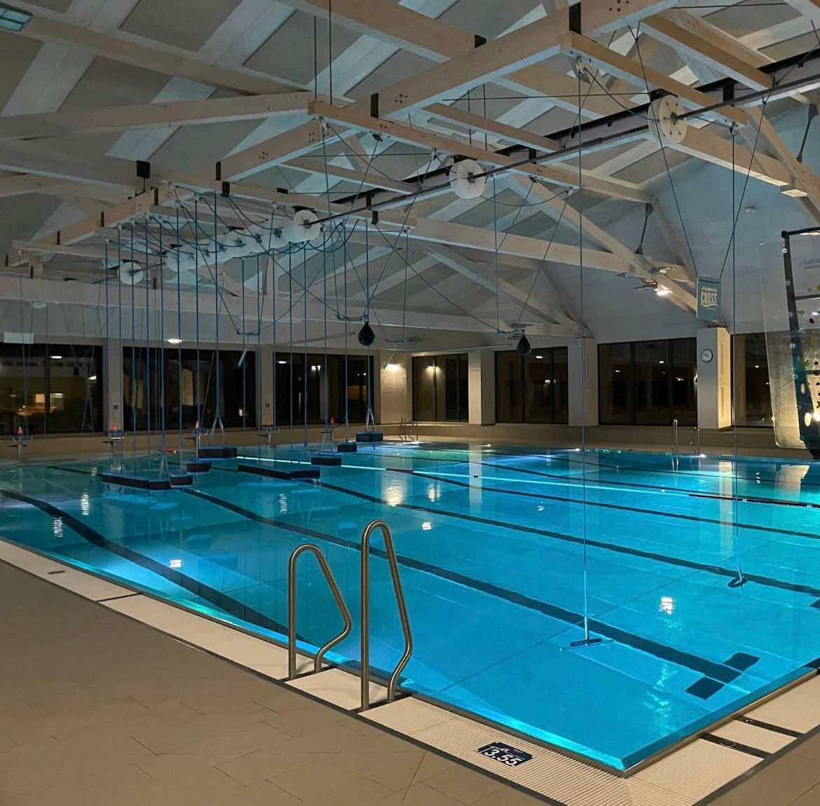 An illuminated indoor swimming pool with an empty pool and a climbing wall in the background.
