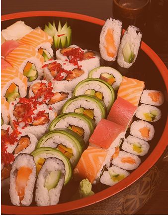 A selection of sushi rolls on a round tray, decorated with wasabi and ginger.