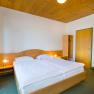 A simply furnished hotel room with a double bed, wooden ceiling, wardrobe and bedside lamps.