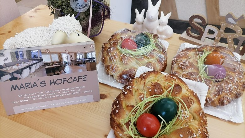 Three Easter wreaths with colorful eggs on a table, next to a card from Maria's Hofcafe and Easter decorations.