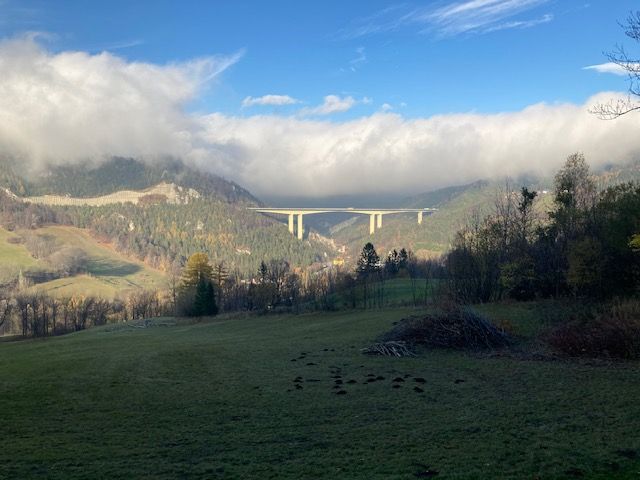 Landscape with bridge over a valley, surrounded by wooded hills and clouds.