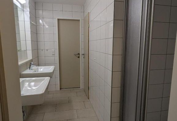 A bathroom with two washbasins, white tiles and a door.