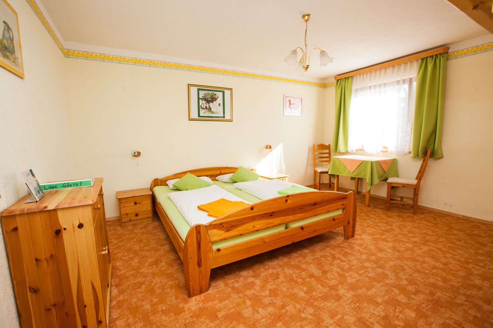 Cozy guest room with wooden furniture, double bed, table and chairs, green curtains and decoration.