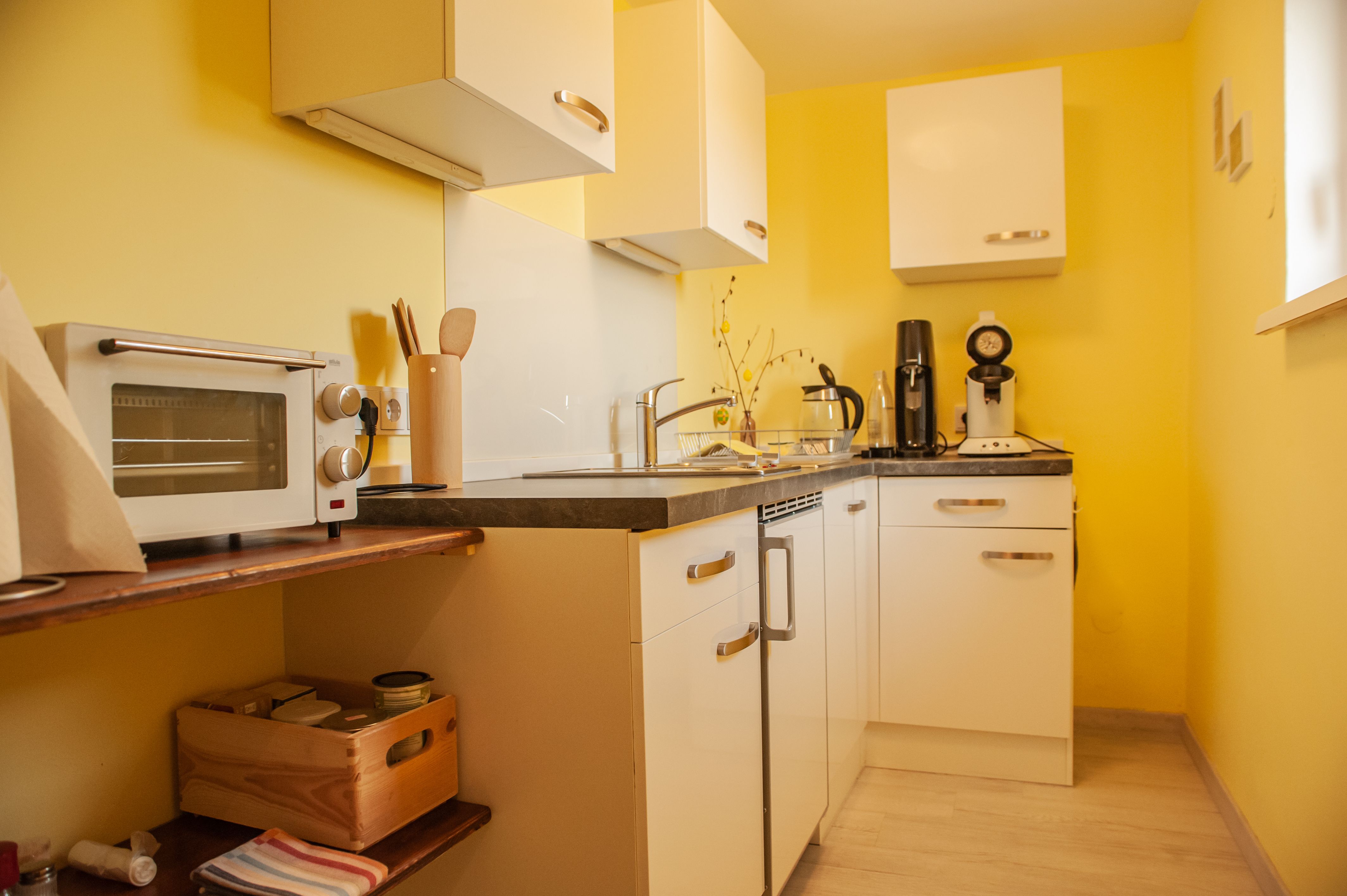 Small kitchen with yellow walls, white cupboards and appliances such as a toaster and coffee machine.