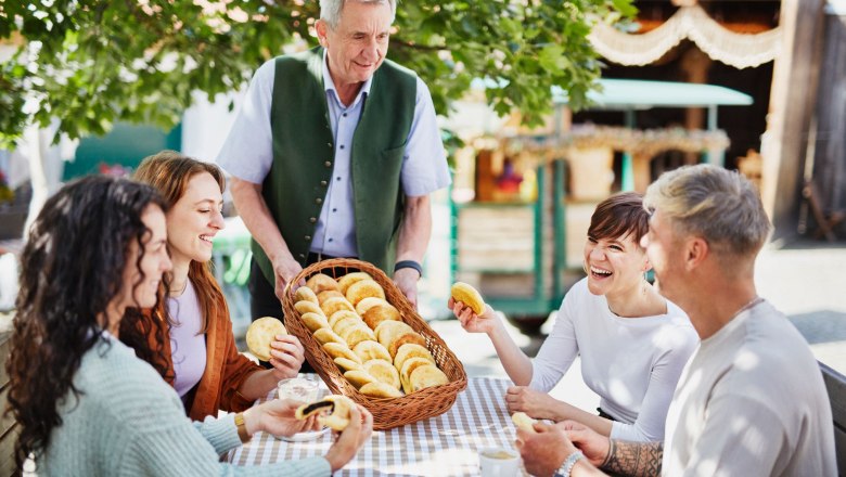 The Mohnwirt serves Mohnzelten to a group of four people at an outdoor table.
