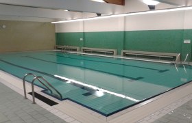 Interior view of an empty indoor pool with green tiled walls and a large swimming pool.