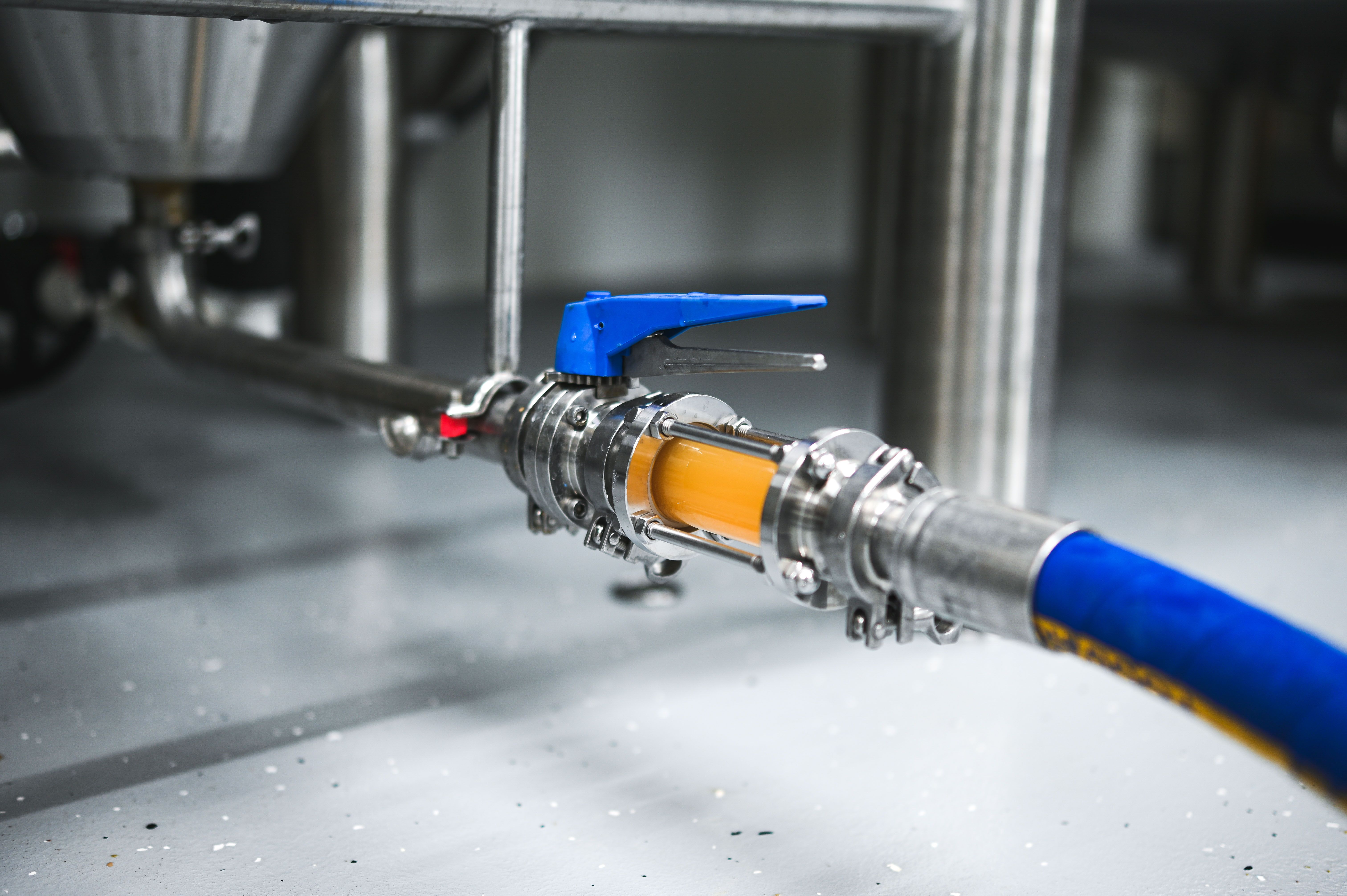 Close-up of a brewery hose with valve and liquid flowing through it.