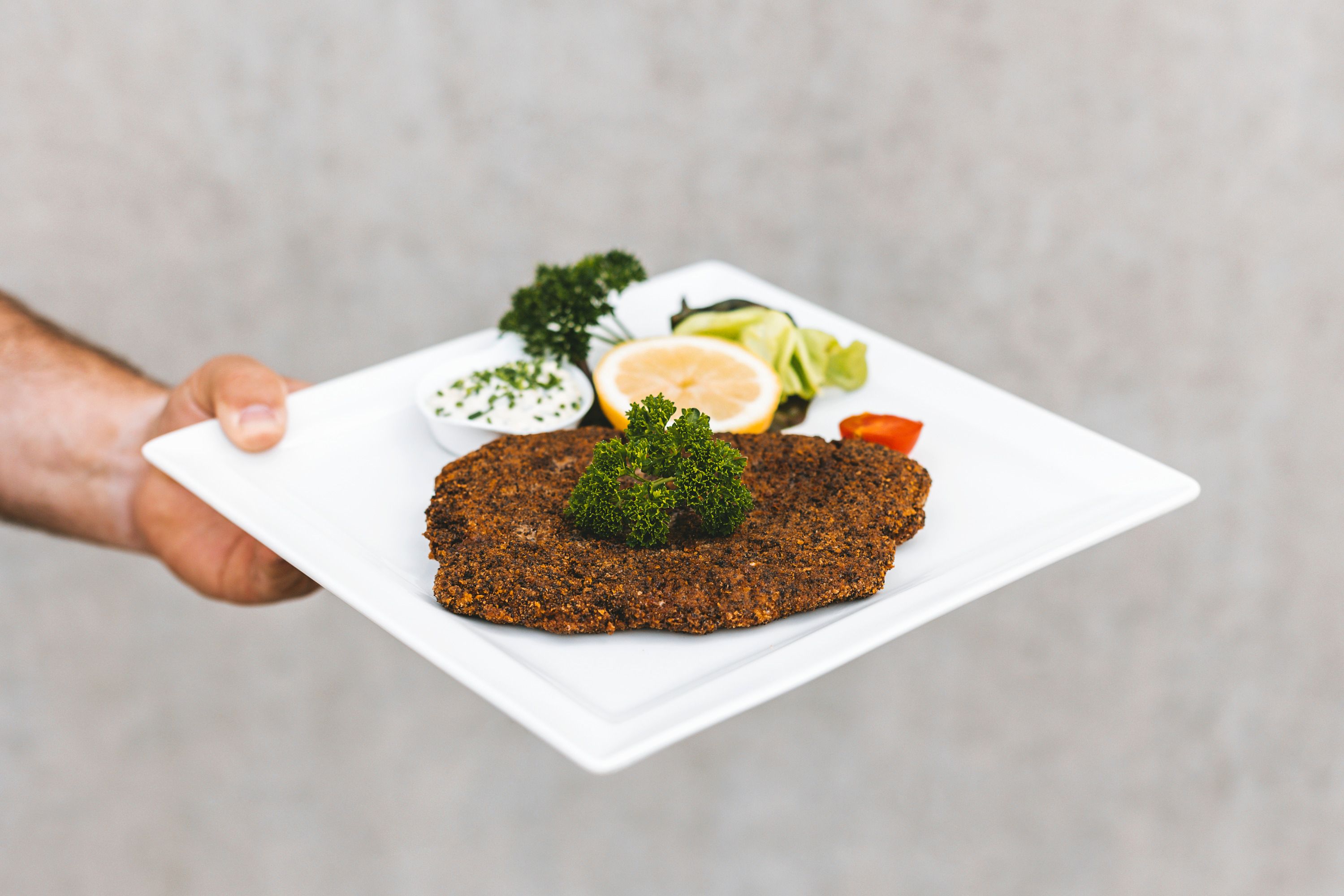 A plate with breaded fish, lemon, parsley and dip.