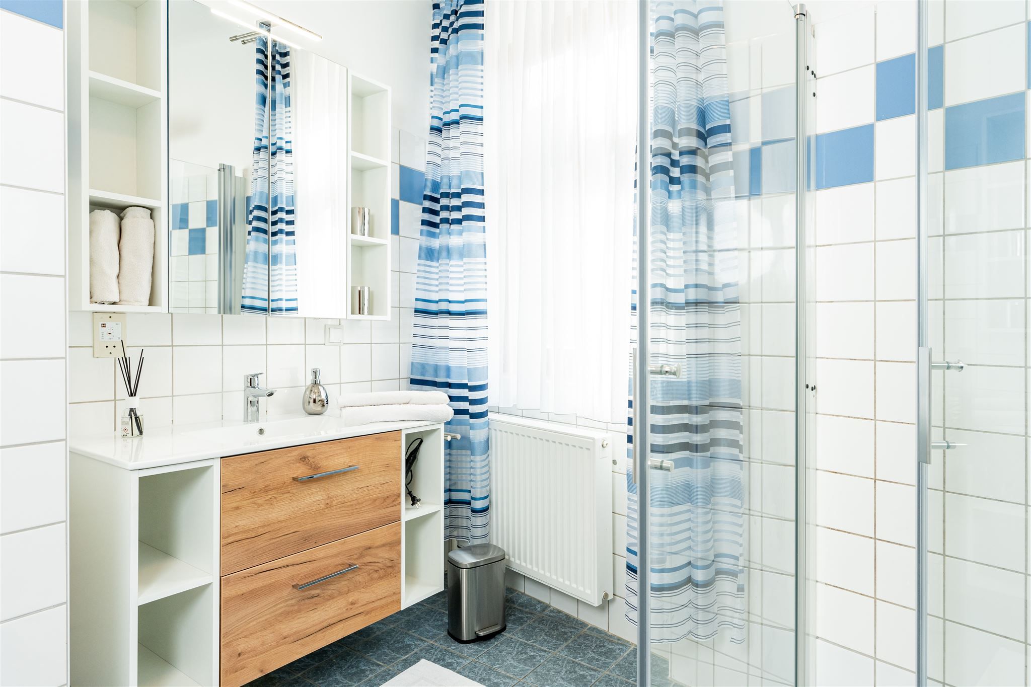 Modern bathroom with wooden cabinet, mirror, shower curtain and tiles.