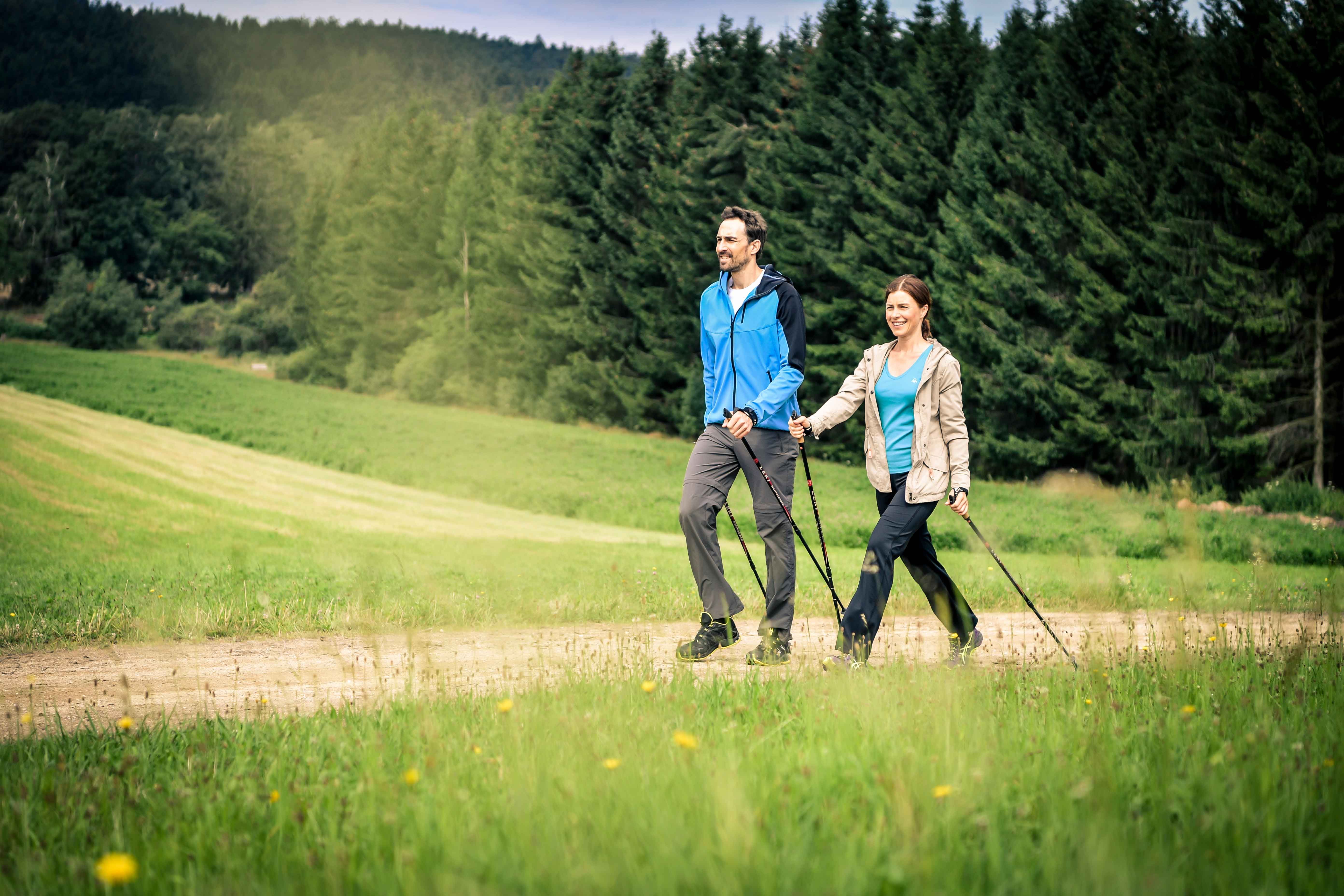 A couple Nordic walking on a country lane in front of a forest.