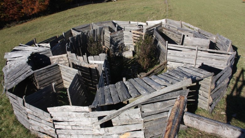 A labyrinth made of wooden planks in a meadow, surrounded by trees in the fall.