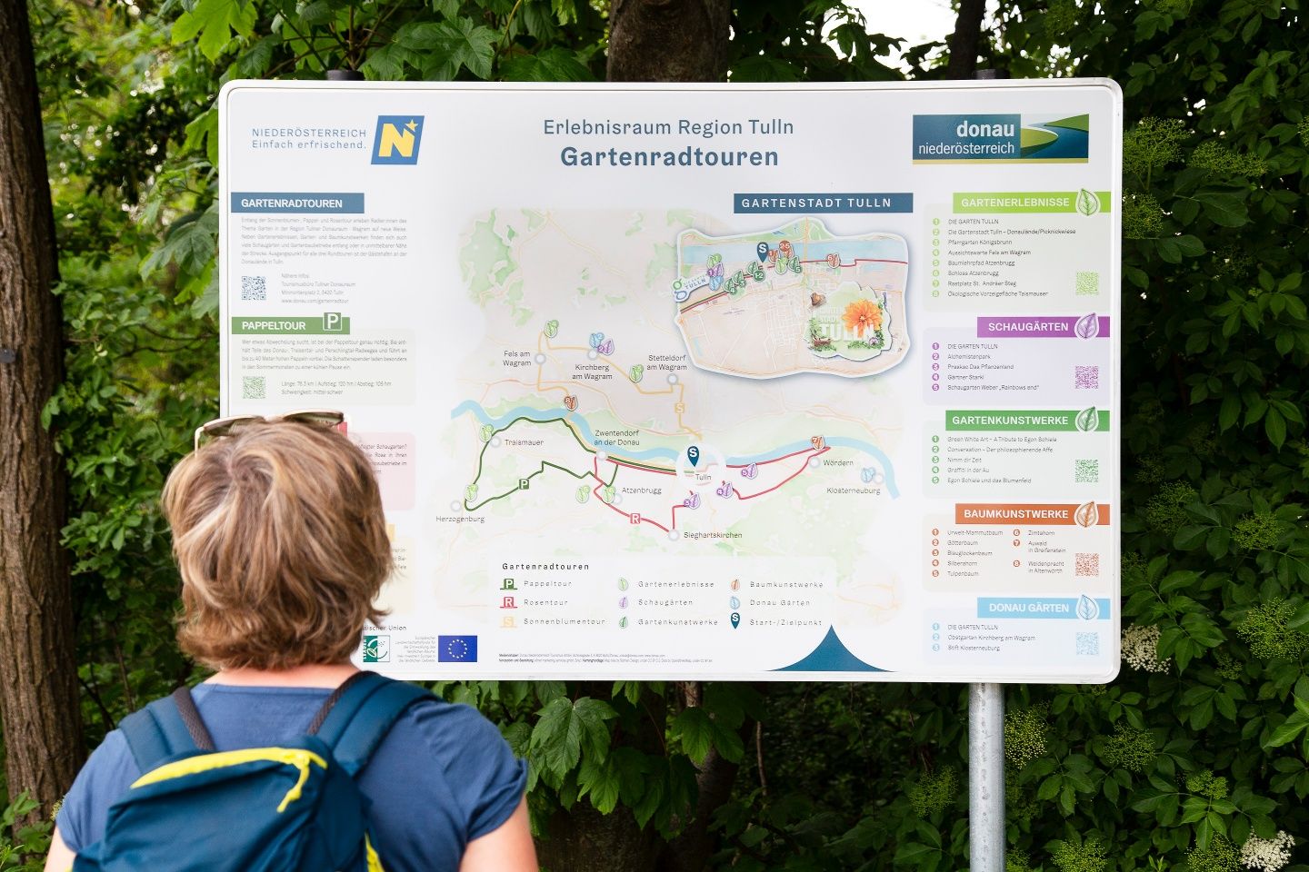A person looks at an information board about garden cycle tours in the Tulln region, Lower Austria, with a map and information on various routes.