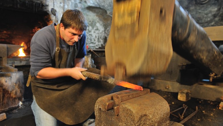 A blacksmith works on red-hot metal with a hammer in a workshop.