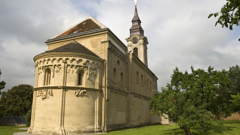 Romanesque church with decorations and tower, surrounded by green meadows and trees.