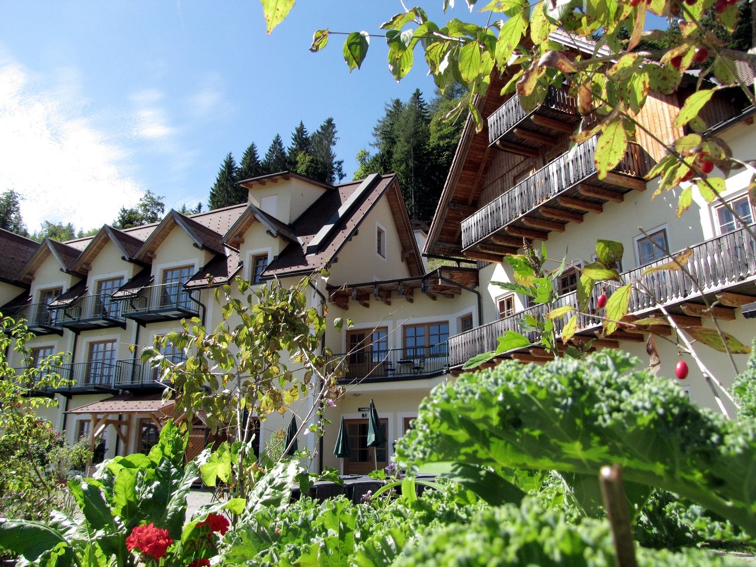 An alpine-style building with balconies, surrounded by lush greenery and plants.
