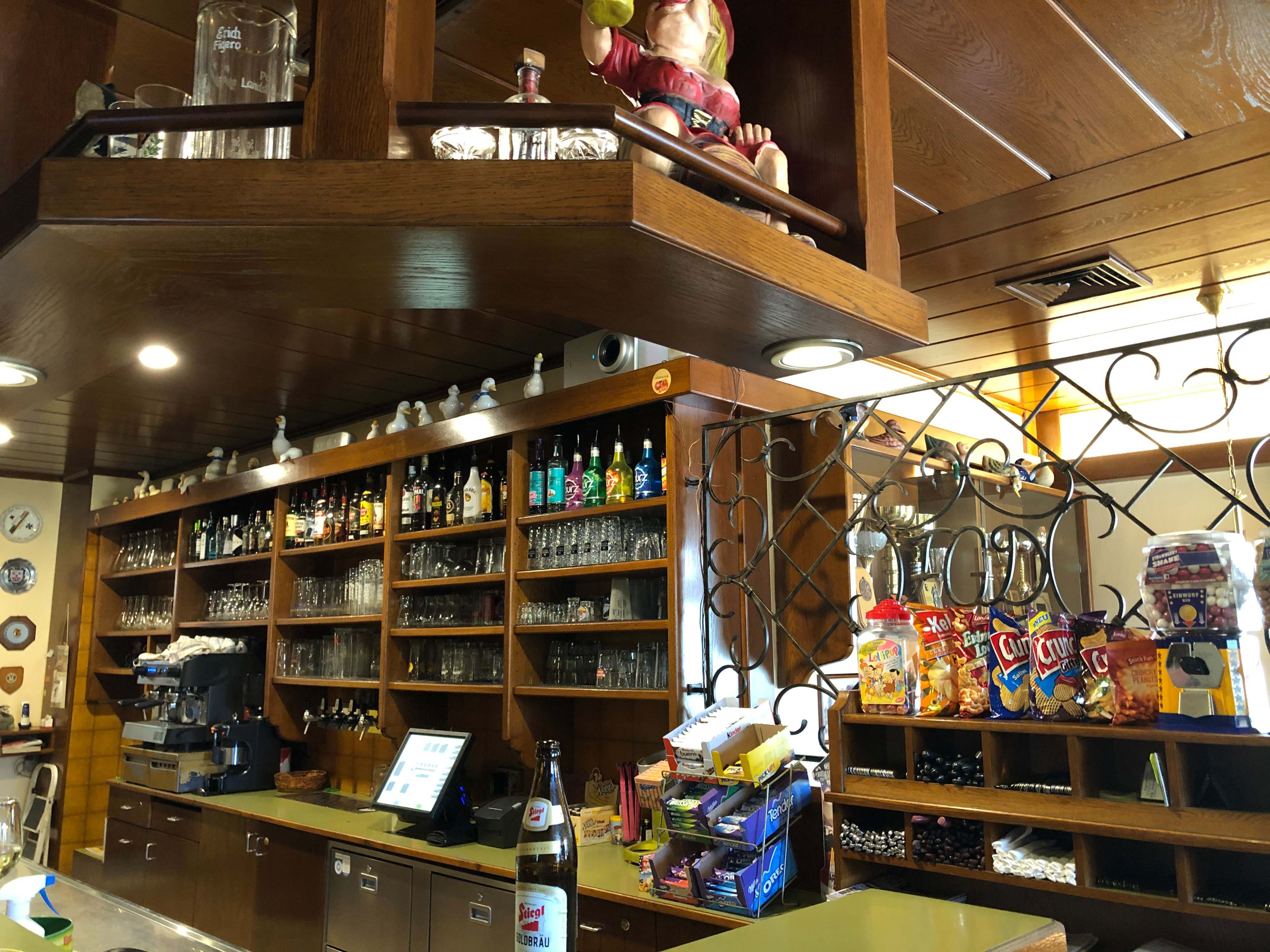 Interior view of a bar with wooden shelves, glasses, bottles and snacks.
