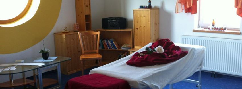 A cozy massage room with massage table, wooden shelves and a large round window.