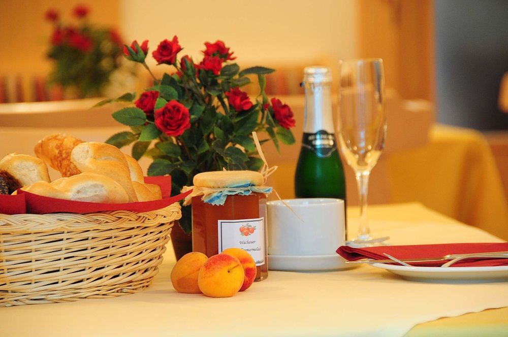 Breakfast table with bread basket, jam, champagne bottle and roses.