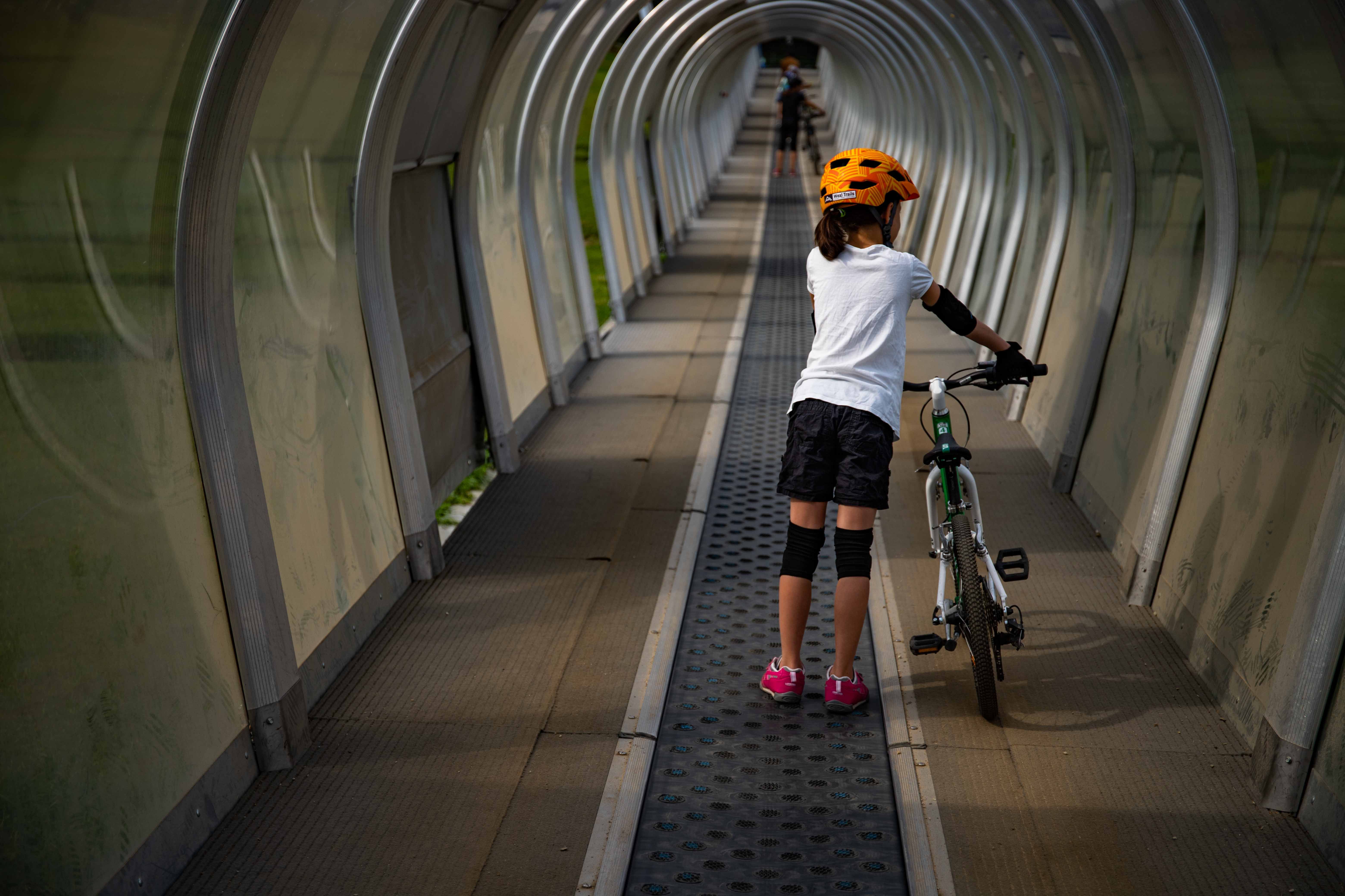 Child with bicycle on conveyor belt in covered tunnel.