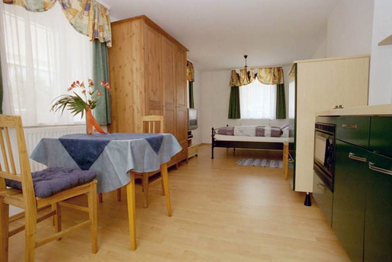 Small apartment with wooden furniture, dining table, chairs, bed and kitchenette.
