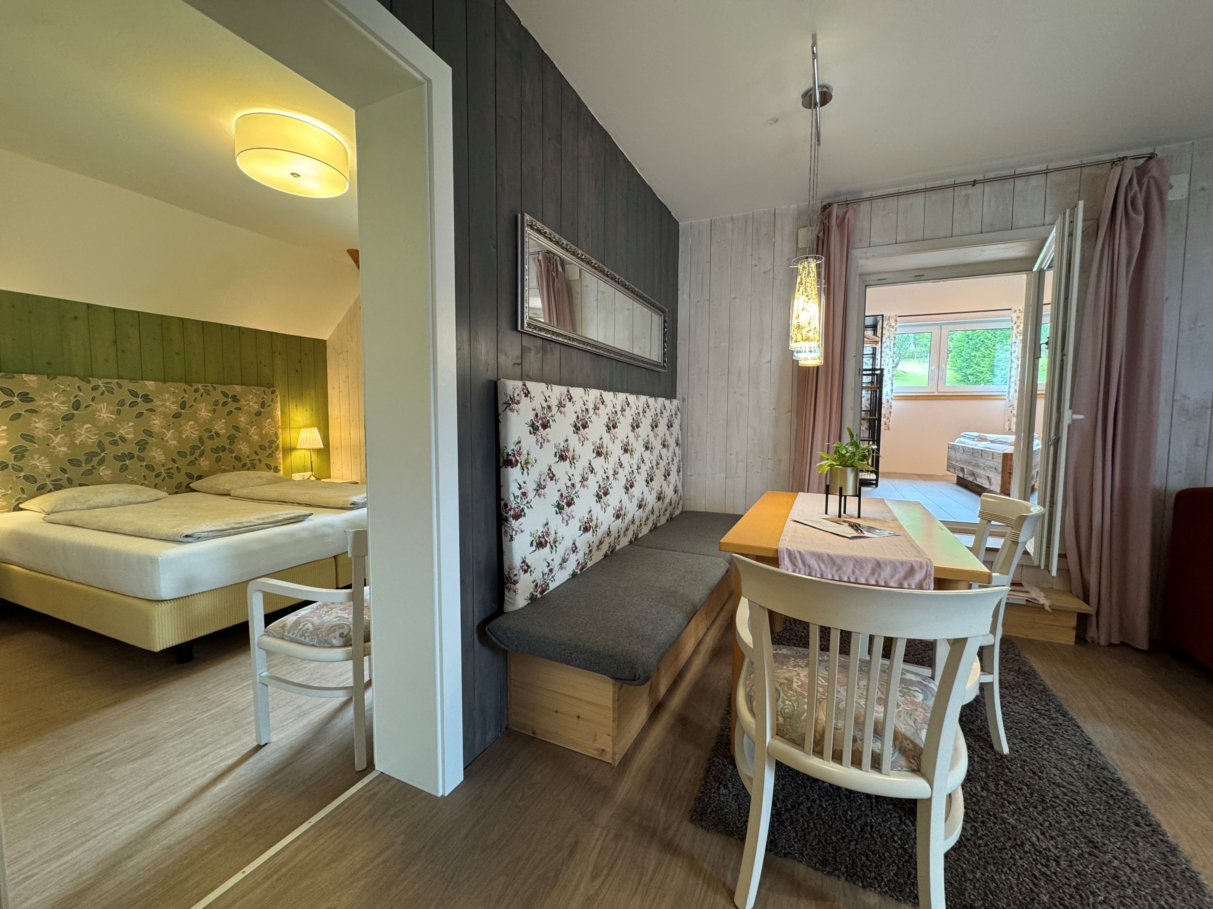 An interior view of a cozy room with a dining table, chairs, and a bed in the background.