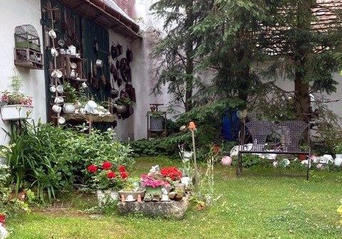 A garden with old pots and decorations on one wall, a flower bed and two chairs.