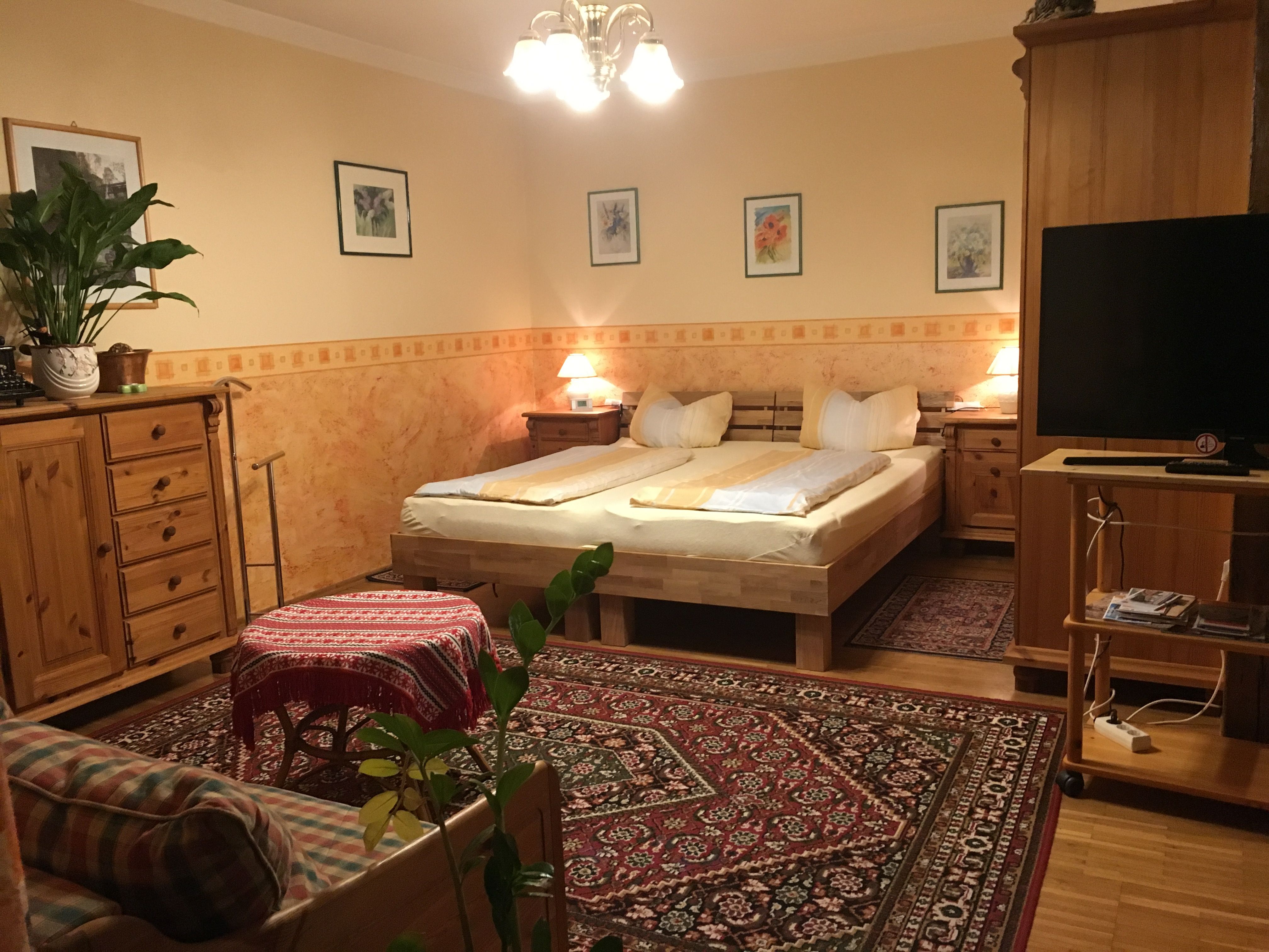 Cozy bedroom with wooden furniture, double bed, carpet and plants.