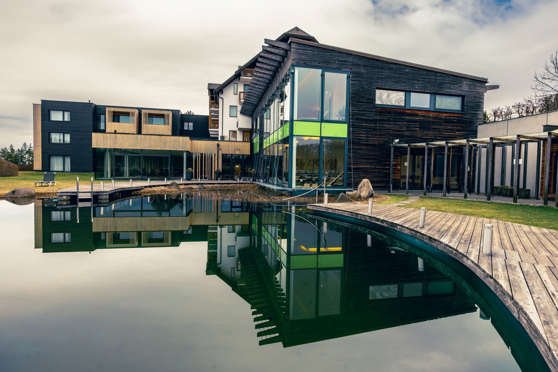 Modern wellness hotel with wooden façade and large pond in the foreground.