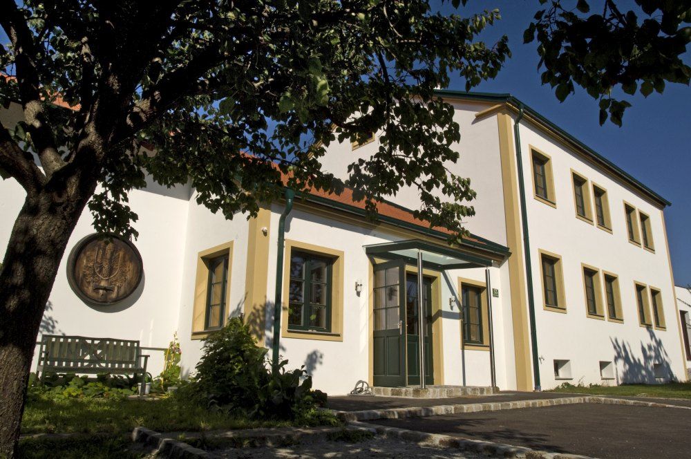 Winery with a white façade and green window frames, surrounded by trees.