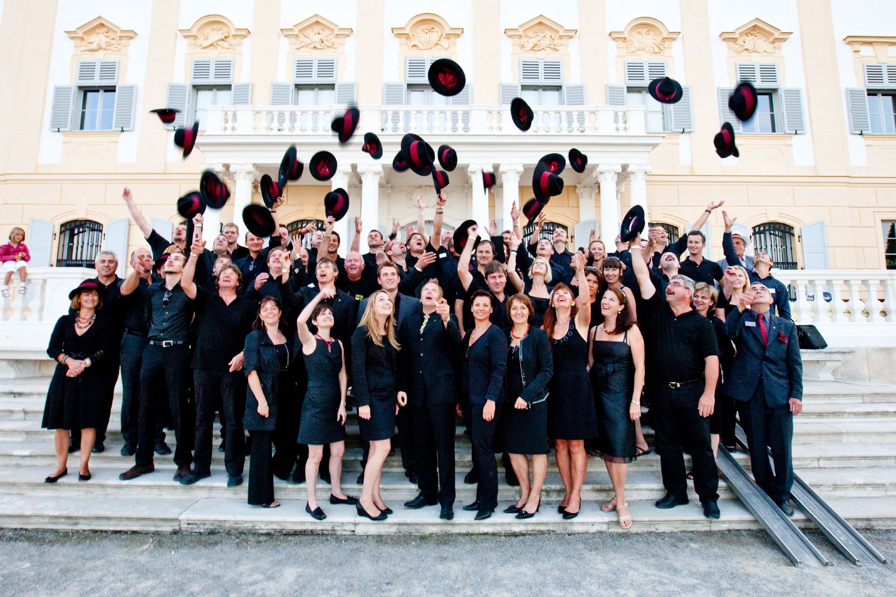 Group of people throwing hats in the air in front of a historic building.