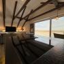 Modern living and dining area with wooden beams, cooking island and large window with a view.