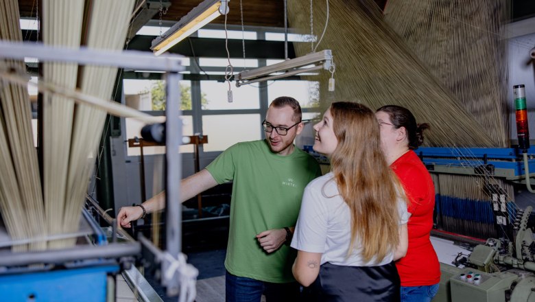 Three people in a textile factory look at a machine.