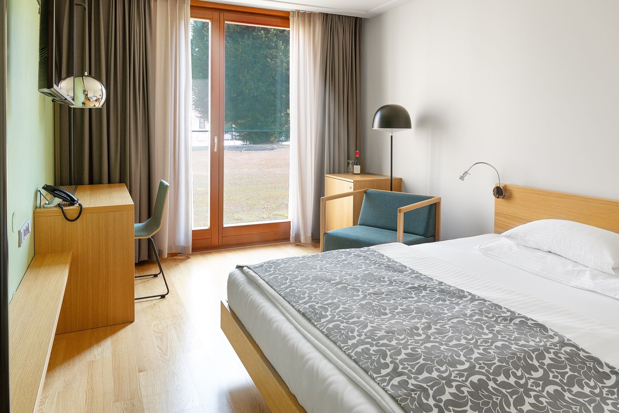 Modern hotel room with wooden furniture, large window and bed.