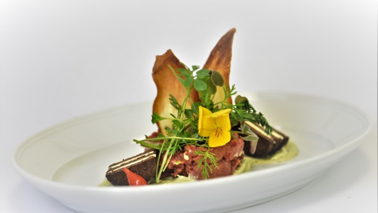 An artfully prepared dish on a white plate decorated with edible flowers and herbs.