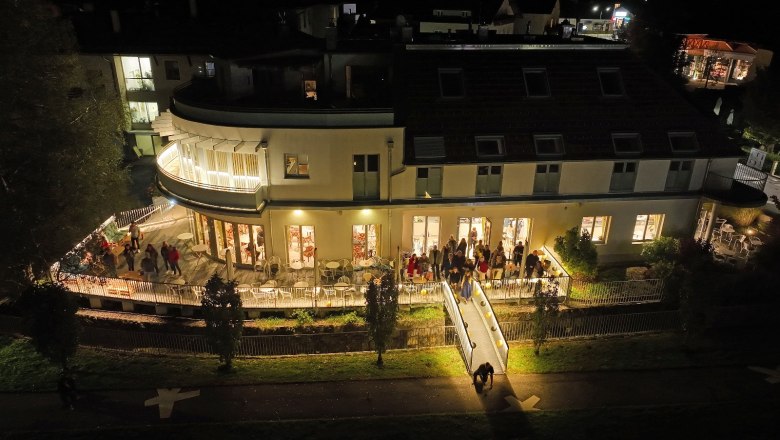 Night shot of the illuminated caf&eacute; with people on the terrace.