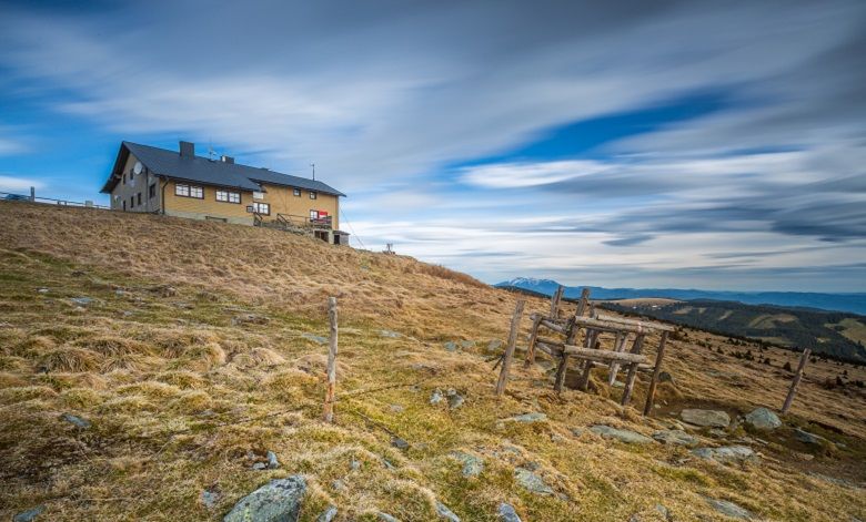 Mountain hut on a hill with a cloudy sky in the background.