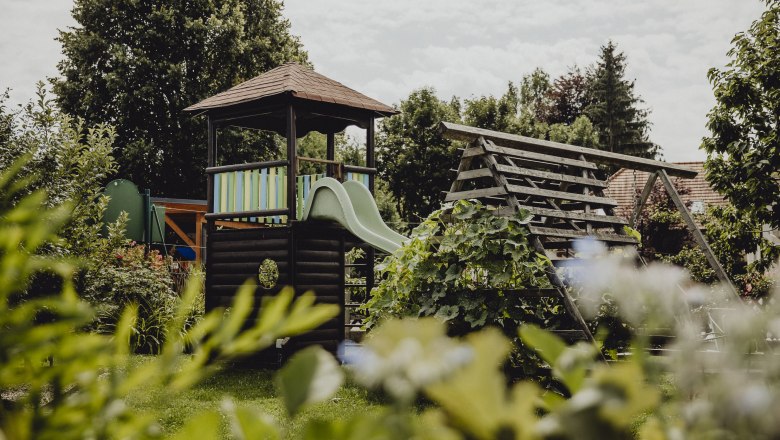 A playground with a slide and climbing frame in a green garden.