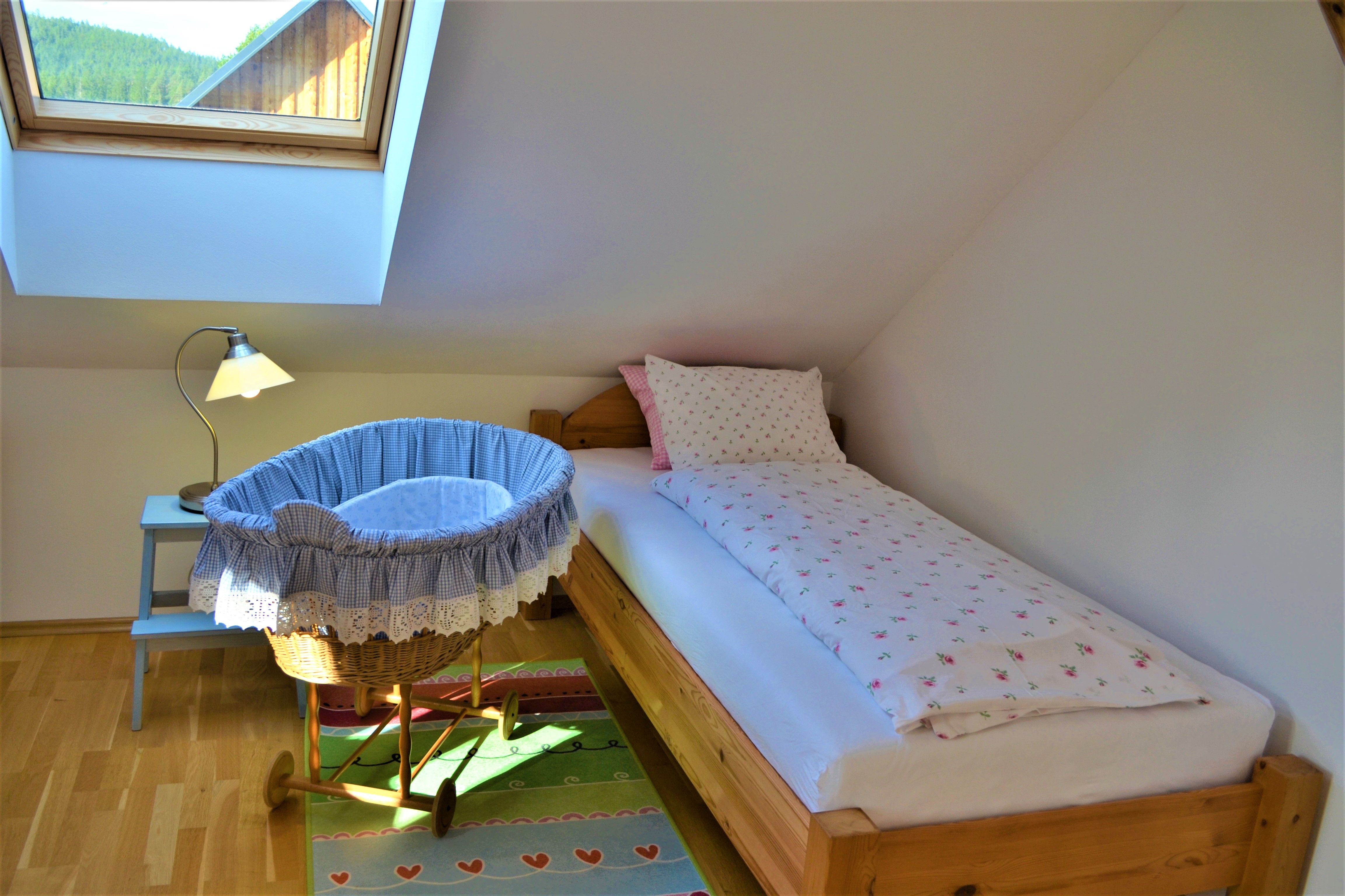A cozy bedroom with single bed, baby cradle and skylight.