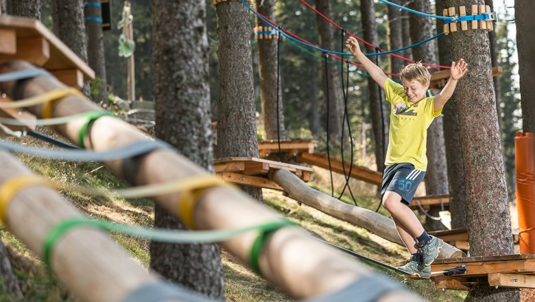 A boy balances on a rope in a climbing park in the forest.