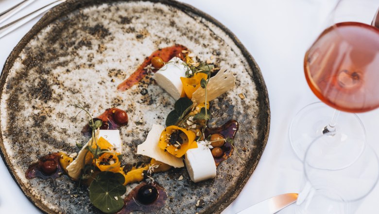 An artfully arranged plate of marinated sheep's cheese, pumpkin and grape salad, with a glass of rosé wine next to it.