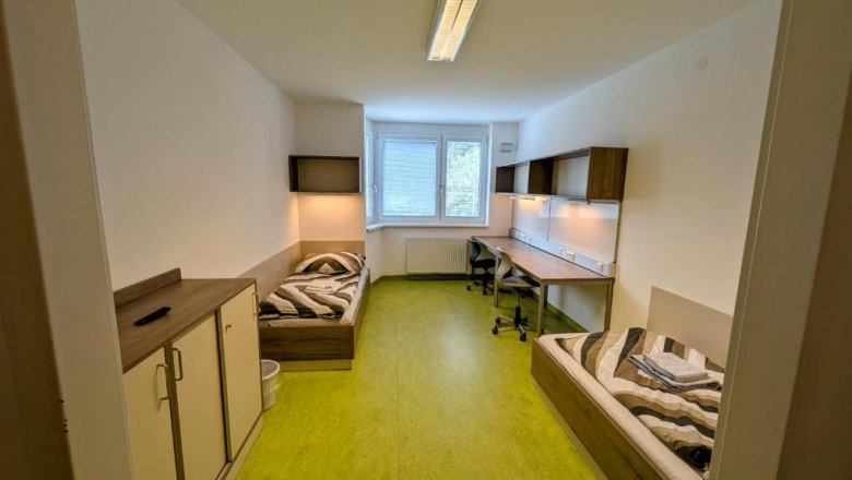 A simply furnished room with two beds, desks and a window.