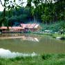 A building with a red roof is reflected in a pond surrounded by trees and meadows.