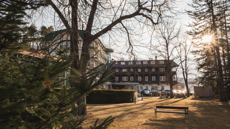 Hotel Schneeberghof in the sunlight with trees in the foreground.